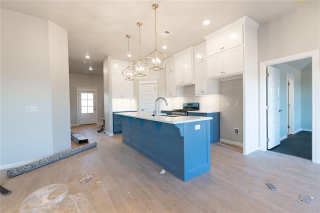 kitchen featuring stainless steel gas stove, light wood finished floors, light countertops, white cabinetry, and a sink