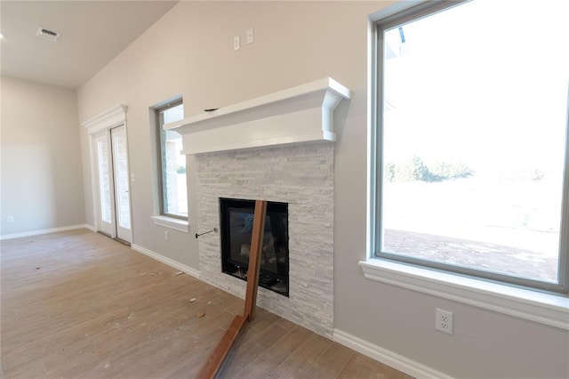 unfurnished living room with baseboards, visible vents, wood finished floors, and a stone fireplace