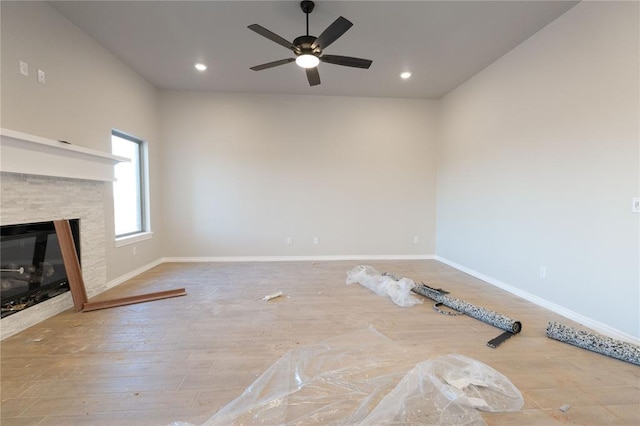 unfurnished living room with recessed lighting, a stone fireplace, baseboards, and wood finished floors