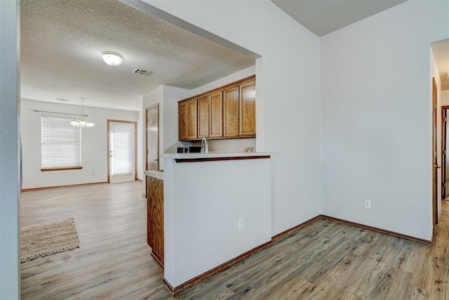 kitchen with pendant lighting, light wood-type flooring, a textured ceiling, and an inviting chandelier