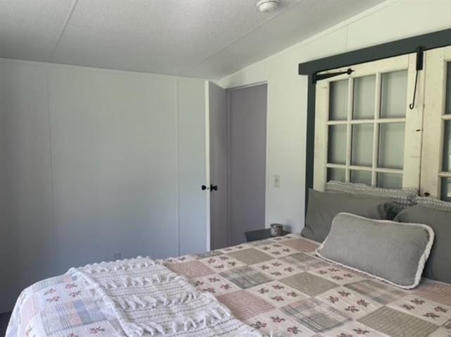 bedroom featuring a barn door, lofted ceiling, and a textured ceiling