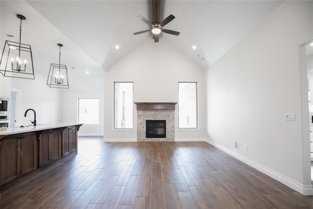 9312 Poppey Pl, Yukon, OK 73099 - unfurnished living room featuring a ceiling fan, high vaulted ceiling, a sink, dark wood finished floors, and a stone fireplace