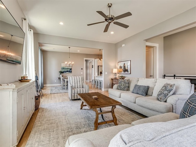 living room featuring ceiling fan with notable chandelier and light wood-type flooring