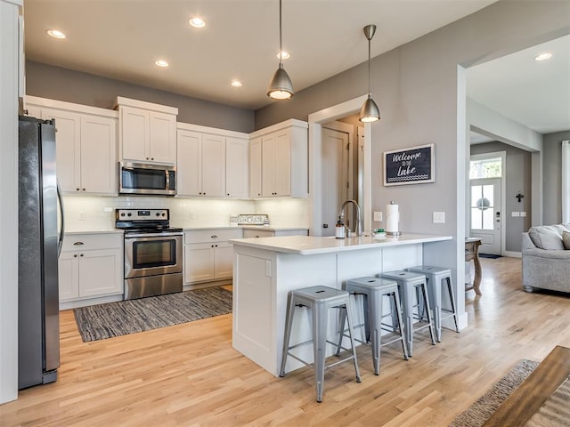 kitchen featuring stainless steel appliances, tasteful backsplash, light hardwood / wood-style floors, decorative light fixtures, and white cabinets