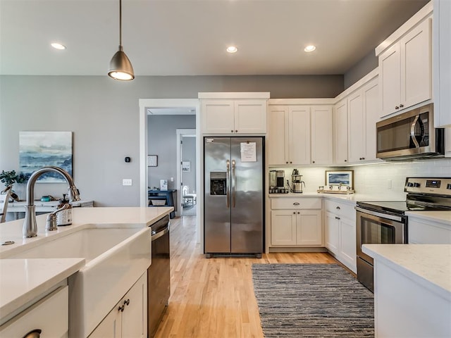 kitchen with decorative light fixtures, light wood-type flooring, white cabinetry, and appliances with stainless steel finishes