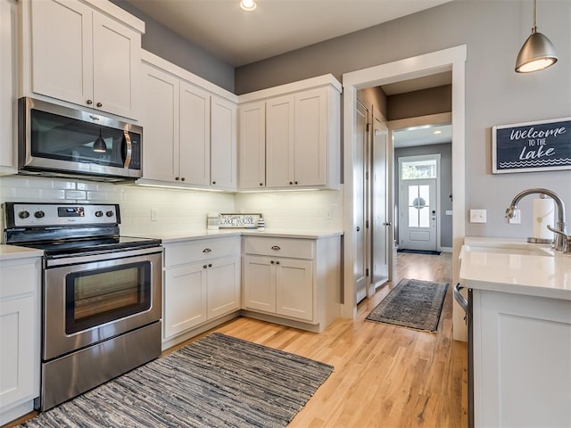 kitchen with white cabinets, sink, decorative backsplash, appliances with stainless steel finishes, and light hardwood / wood-style floors