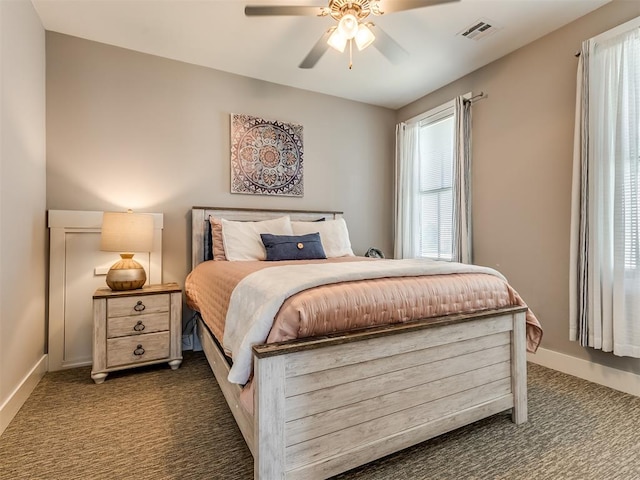 bedroom with multiple windows, dark colored carpet, and ceiling fan