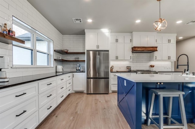 kitchen with stainless steel refrigerator, white cabinetry, hanging light fixtures, light hardwood / wood-style flooring, and decorative backsplash