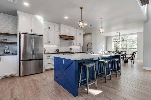 kitchen with hanging light fixtures, an island with sink, a kitchen bar, white cabinetry, and stainless steel refrigerator