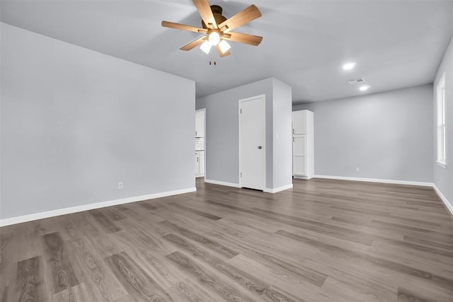 spare room featuring a ceiling fan, visible vents, baseboards, and wood finished floors
