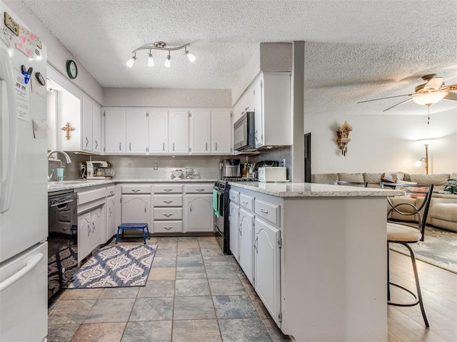 kitchen featuring kitchen peninsula, a textured ceiling, a breakfast bar area, white cabinets, and black appliances