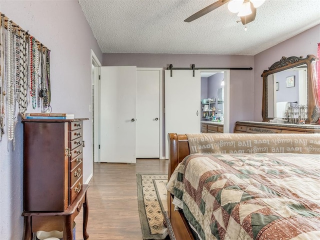 bedroom featuring ceiling fan, a barn door, light hardwood / wood-style floors, and a textured ceiling