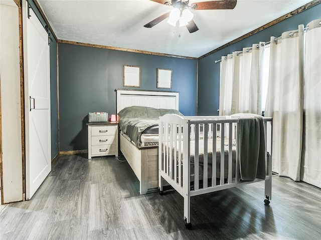 bedroom featuring a barn door, ceiling fan, hardwood / wood-style floors, and crown molding