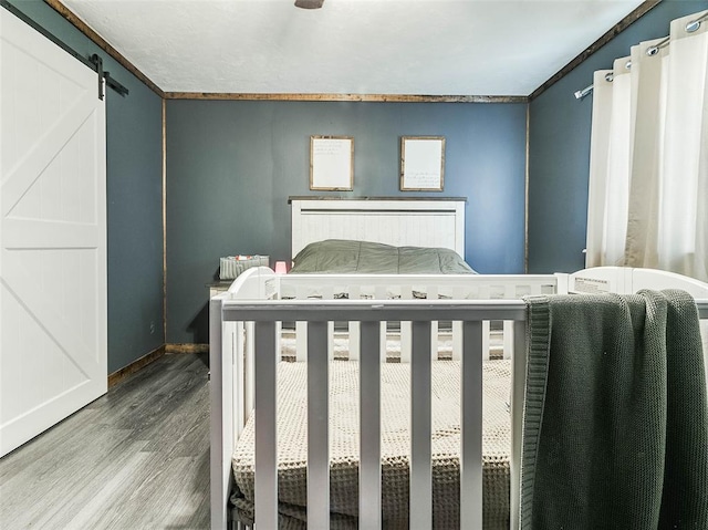 bedroom with a barn door, hardwood / wood-style flooring, and ornamental molding