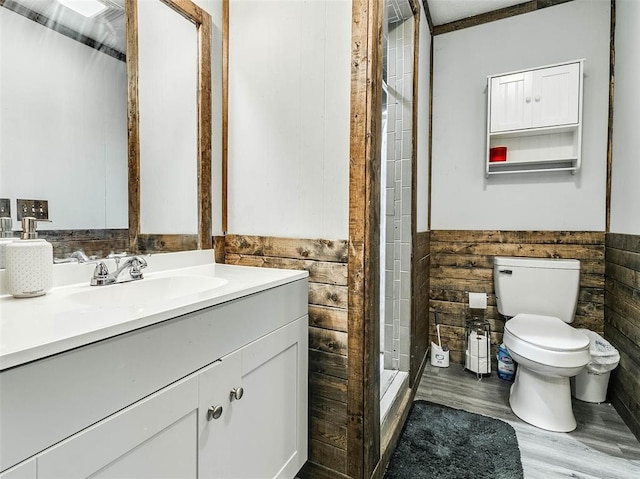 bathroom with vanity, wooden walls, tiled shower, hardwood / wood-style floors, and toilet