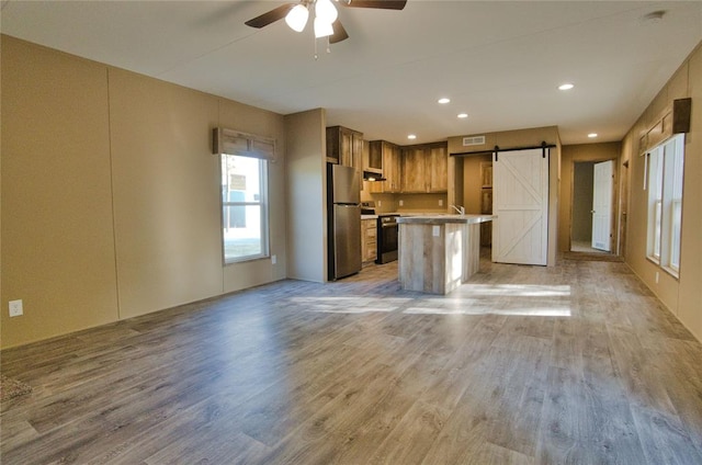 kitchen featuring light hardwood / wood-style flooring, a barn door, a kitchen island, a kitchen bar, and stainless steel appliances