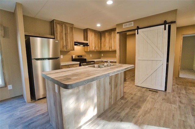 kitchen featuring sink, stainless steel appliances, a barn door, light hardwood / wood-style flooring, and a kitchen island with sink