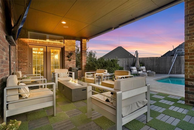 patio terrace at dusk with a fenced in pool, french doors, and an outdoor living space with a fire pit