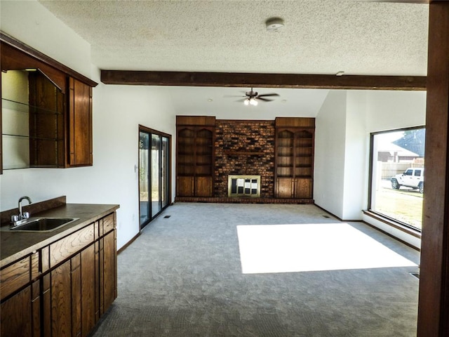 interior space with a textured ceiling, light colored carpet, ceiling fan, sink, and beam ceiling