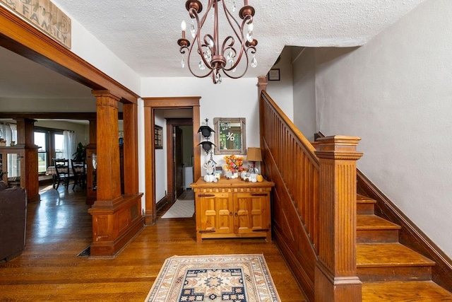 stairway with decorative columns, wood-type flooring, a textured ceiling, and an inviting chandelier