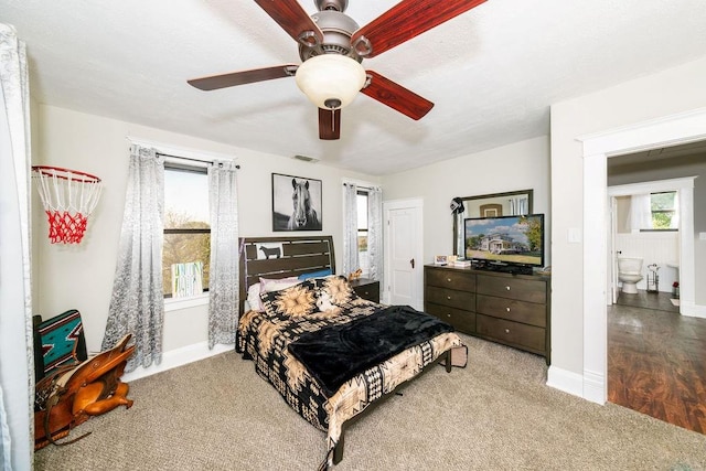 bedroom featuring multiple windows, hardwood / wood-style flooring, ensuite bath, and ceiling fan