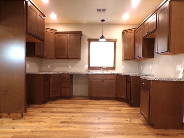 kitchen featuring light stone counters, sink, hanging light fixtures, and light wood-type flooring