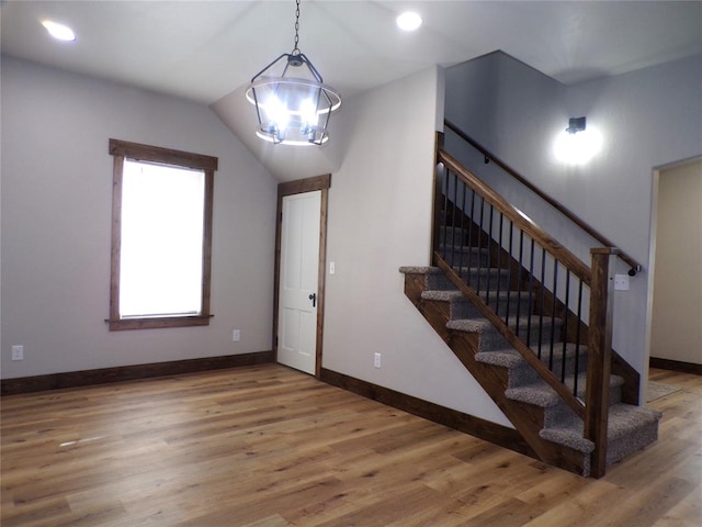 staircase featuring hardwood / wood-style floors, an inviting chandelier, and lofted ceiling