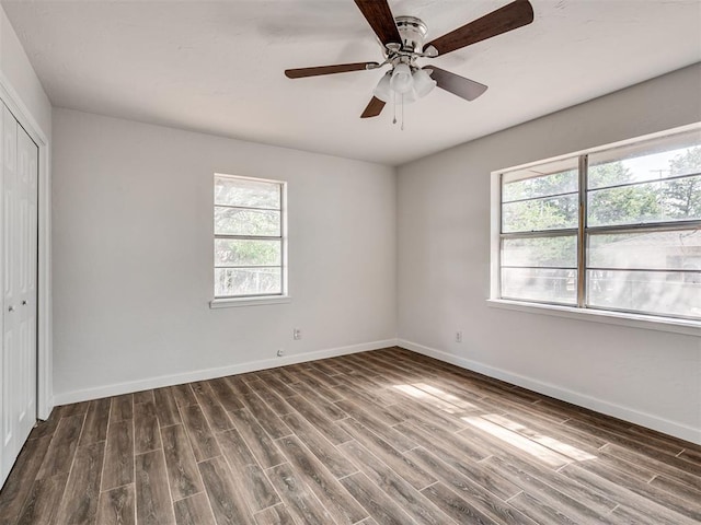 unfurnished bedroom with a closet, dark hardwood / wood-style floors, multiple windows, and ceiling fan