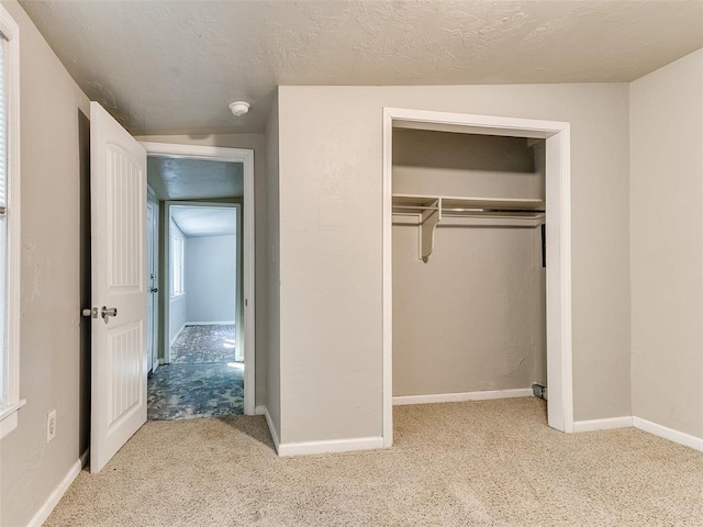 unfurnished bedroom featuring a textured ceiling, light colored carpet, a closet, and lofted ceiling