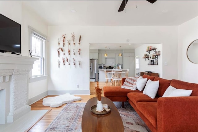 living room featuring a brick fireplace, ceiling fan, and light hardwood / wood-style flooring