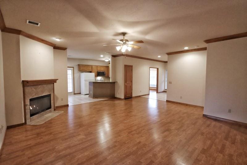 unfurnished living room with a premium fireplace, crown molding, ceiling fan, and light hardwood / wood-style floors