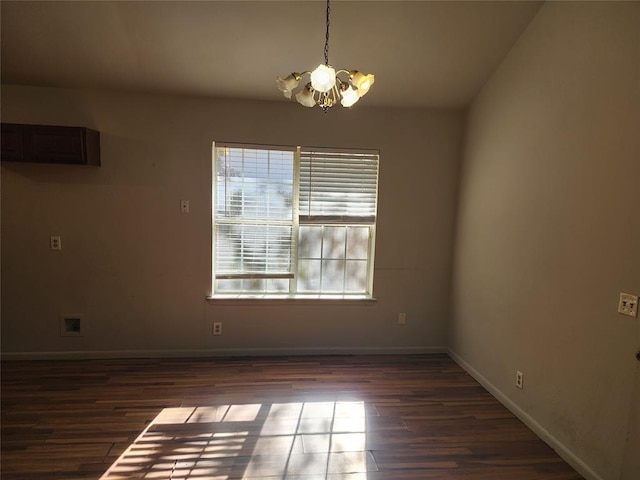 empty room featuring lofted ceiling, dark wood-type flooring, and an inviting chandelier