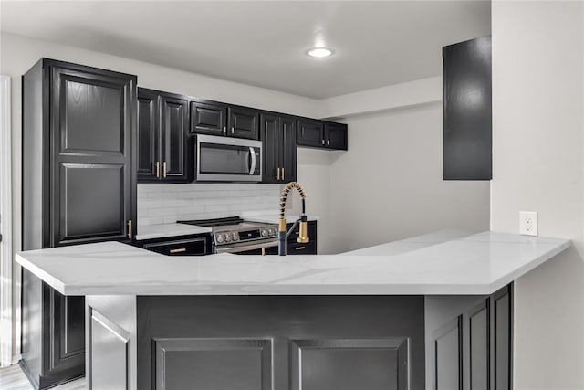 kitchen featuring light stone counters, kitchen peninsula, backsplash, and appliances with stainless steel finishes