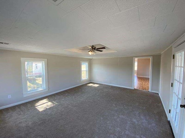 spare room with dark colored carpet, ceiling fan, and a raised ceiling