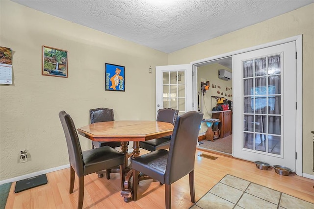 dining space featuring a textured ceiling, light hardwood / wood-style floors, and an AC wall unit