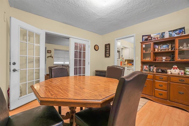 dining room featuring a textured ceiling, light wood-type flooring, and french doors