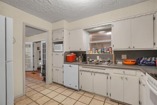 kitchen featuring sink, light tile patterned flooring, a textured ceiling, white appliances, and white cabinets