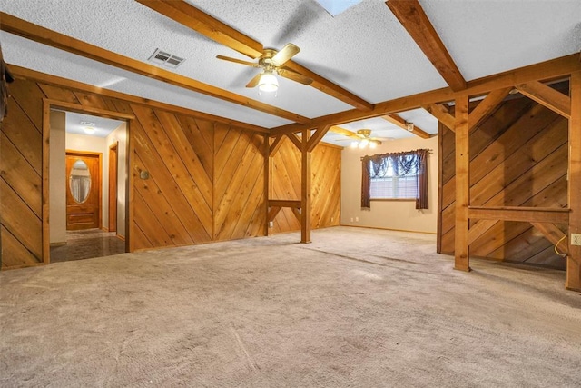 unfurnished living room featuring wood walls, ceiling fan, a textured ceiling, beamed ceiling, and carpet floors