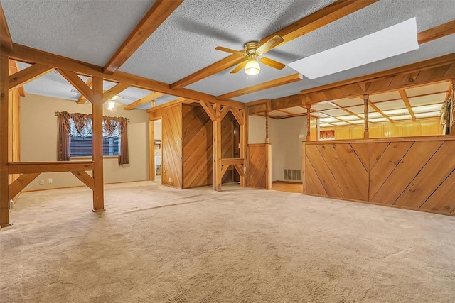 unfurnished living room featuring wooden walls, beamed ceiling, carpet floors, and a textured ceiling