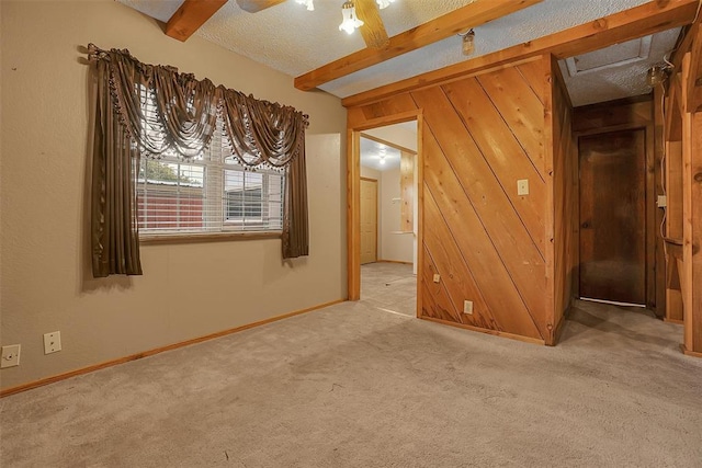 empty room featuring beam ceiling, ceiling fan, wooden walls, a textured ceiling, and light carpet