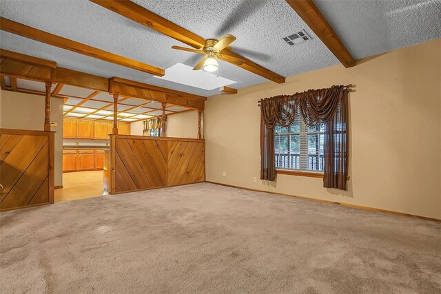 interior space with beam ceiling, light carpet, ceiling fan, and a textured ceiling