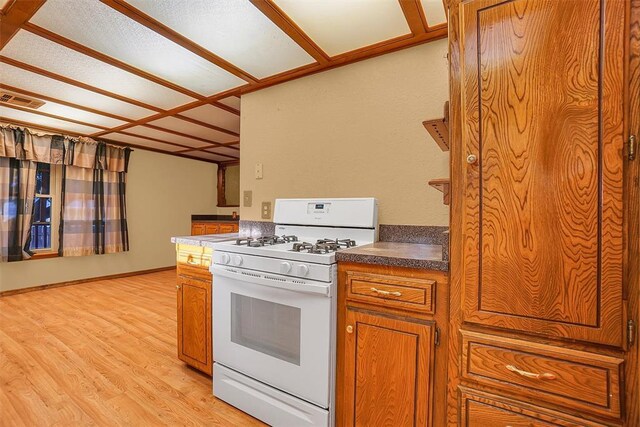 420 W 8th St, Cordell, OK 73632 - kitchen with white range with gas stovetop, brown cabinetry, light wood-style floors, and dark countertops