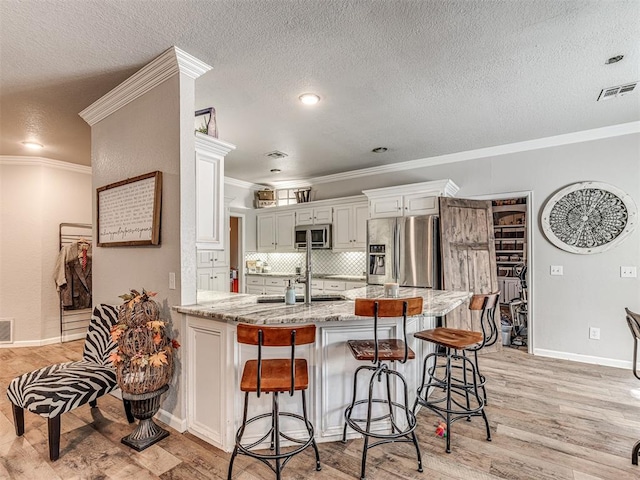 kitchen with light stone countertops, stainless steel appliances, white cabinetry, and light hardwood / wood-style floors