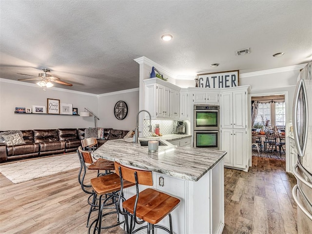 kitchen featuring light stone countertops, appliances with stainless steel finishes, light wood-type flooring, ceiling fan, and sink