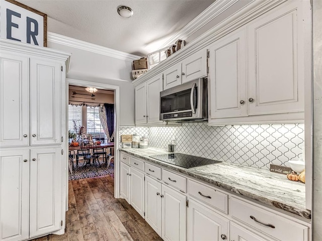 kitchen featuring backsplash, wood-type flooring, black electric cooktop, white cabinets, and ornamental molding