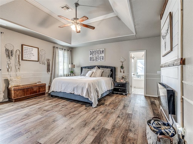 bedroom featuring hardwood / wood-style flooring, ensuite bath, ceiling fan, and a tray ceiling