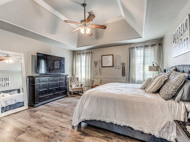 bedroom with wood-type flooring, a textured ceiling, a raised ceiling, and ceiling fan