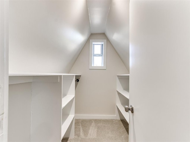 walk in closet with light colored carpet and lofted ceiling