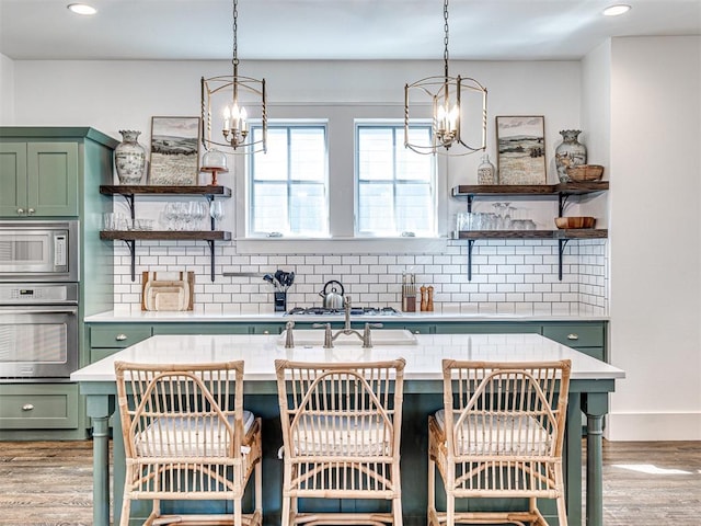 kitchen with decorative backsplash, wood-type flooring, stainless steel appliances, and green cabinetry