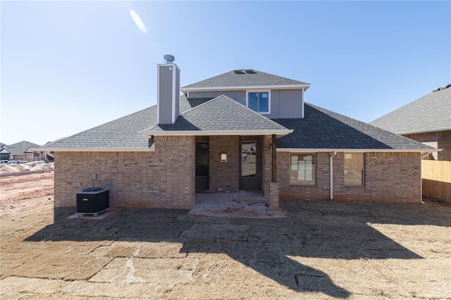 rear view of property featuring brick siding, central air condition unit, a shingled roof, and a patio